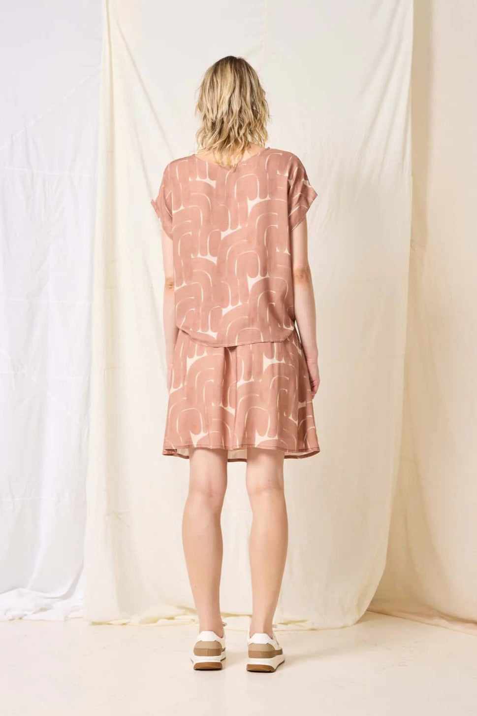 Person wearing a pink patterned outfit standing in front of white curtains