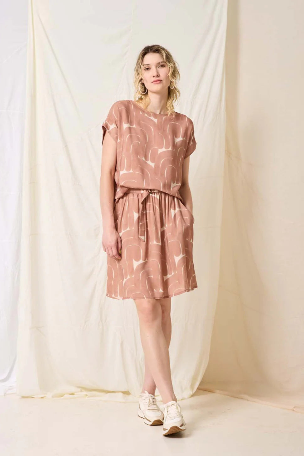 Woman wearing a pink patterned outfit against a white curtain background