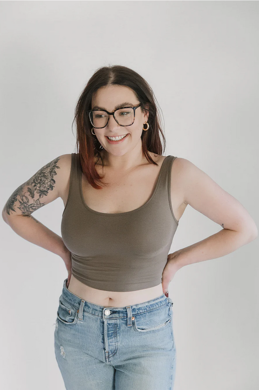 A woman wearing the Primrose Crop Tank by Blondie Apparel  in Clay with jeans, standing in front of a white background 