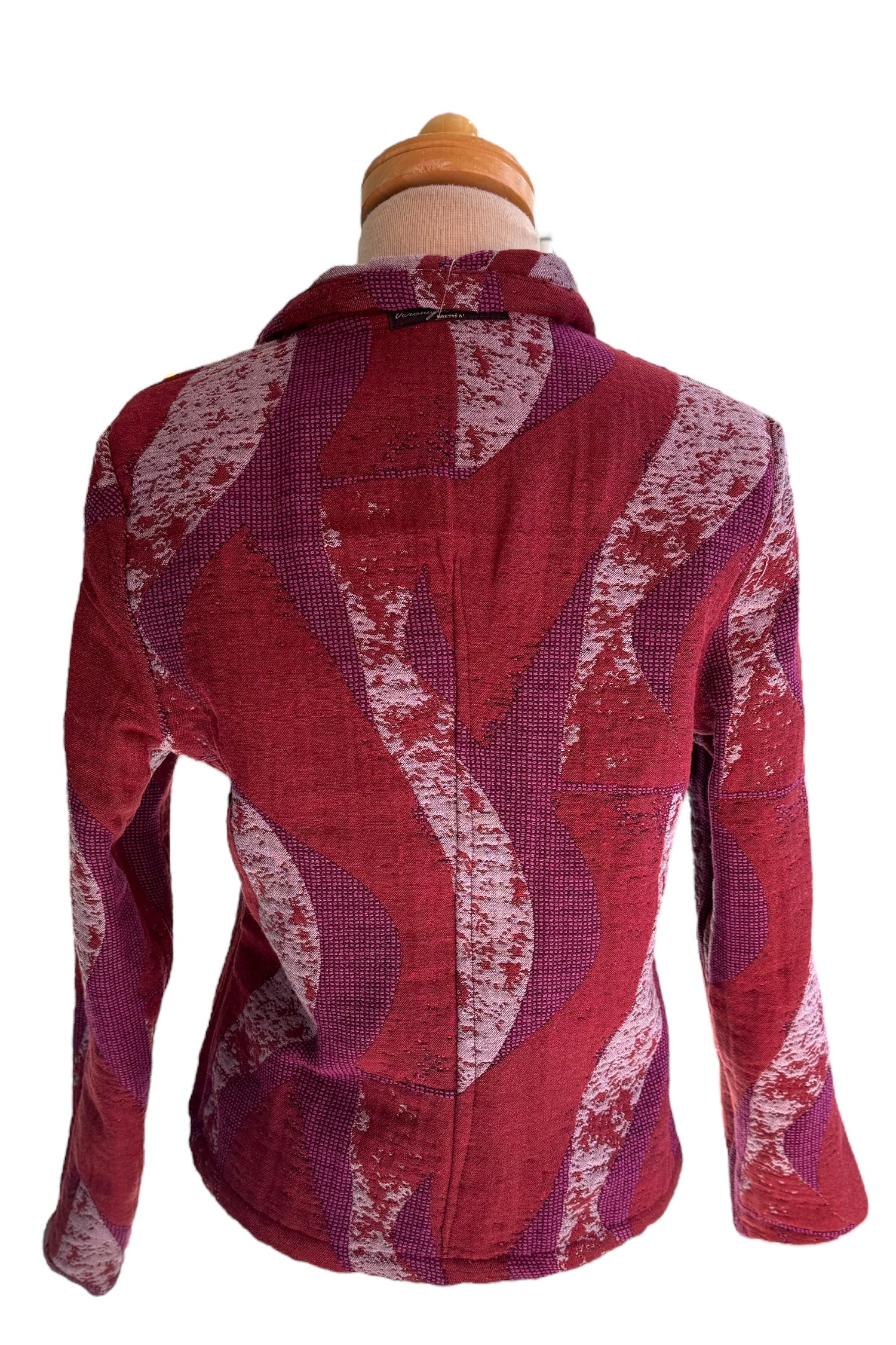 A back view of the Reversible Short Bomber Jacket by Véronique d’Aragon in purple, a cropped jacket with a classic collar and a zip front that's reversible inside out, is show on a mannequin against a white background. 