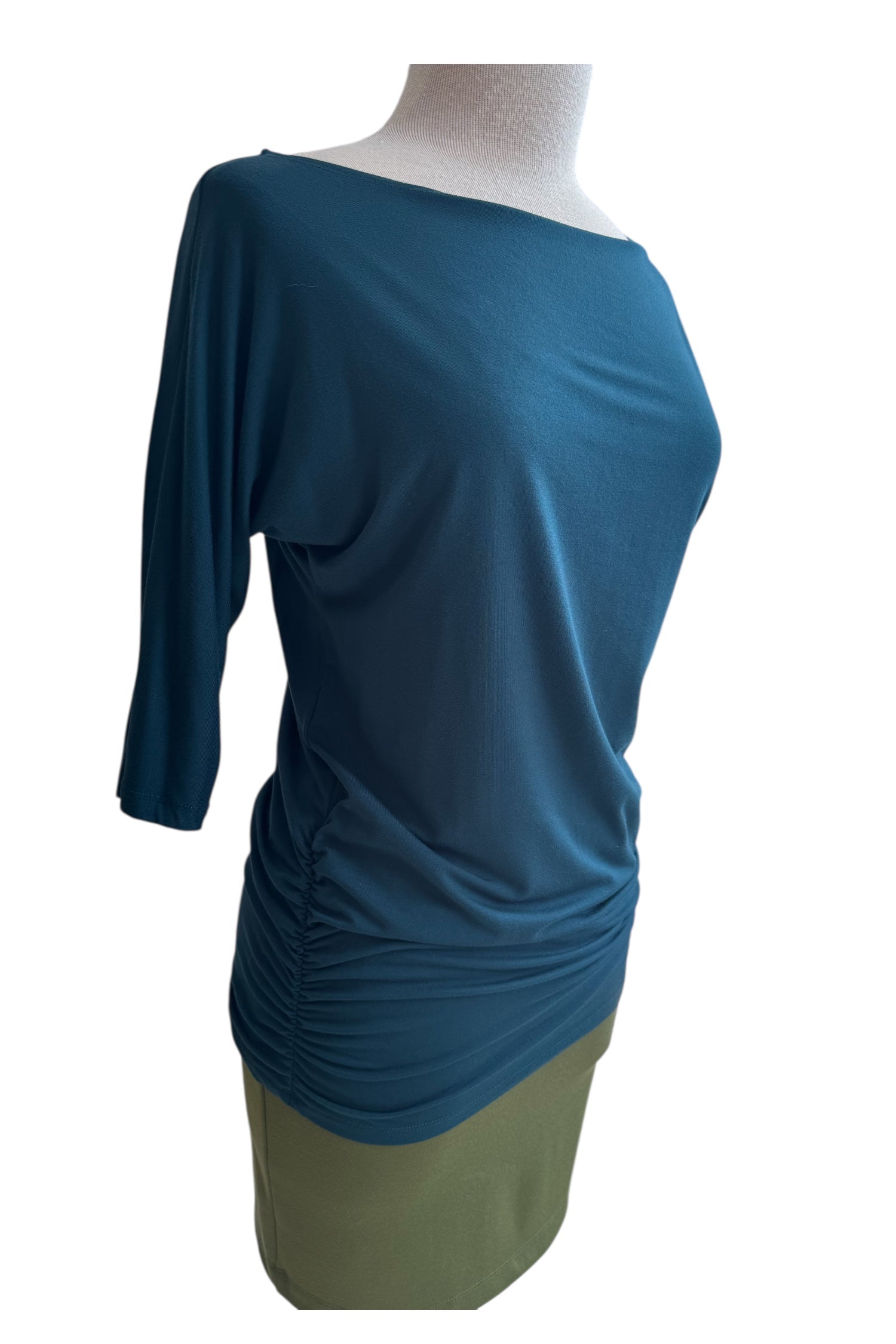 A side view of the Bettina Top by MOOVment in Teat, with boat neck, 3/4 sleeves, and gathered sides, is shown with a green skirt on a mannequin in front of a white background. 