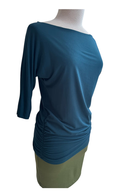 A side view of the Bettina Top by MOOVment in Teat, with boat neck, 3/4 sleeves, and gathered sides, is shown with a green skirt on a mannequin in front of a white background. 