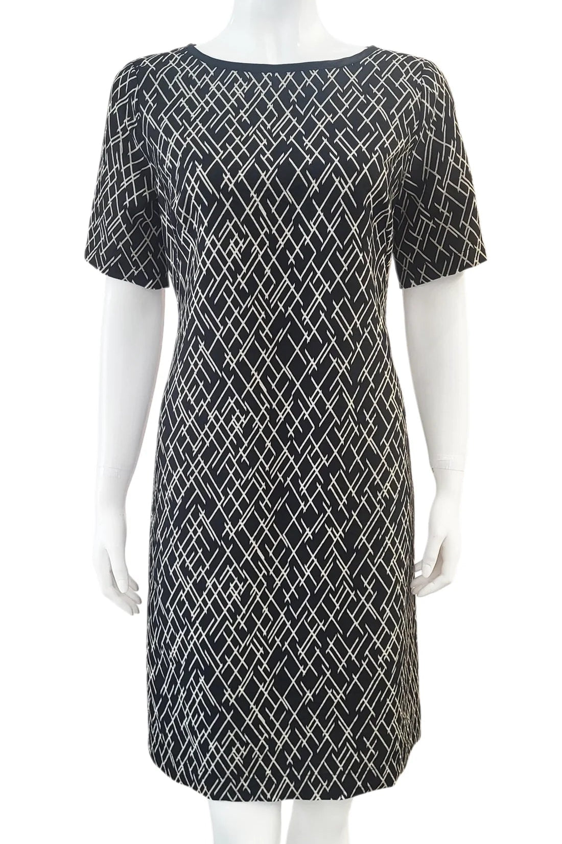 The Cecily Simple Shift Dress from Mandala in Crosstown print is shown on a mannequin against a white background. It has a high neck, short sleeves, a knee-length hem, French darts, and elastic at the back of the waist. 