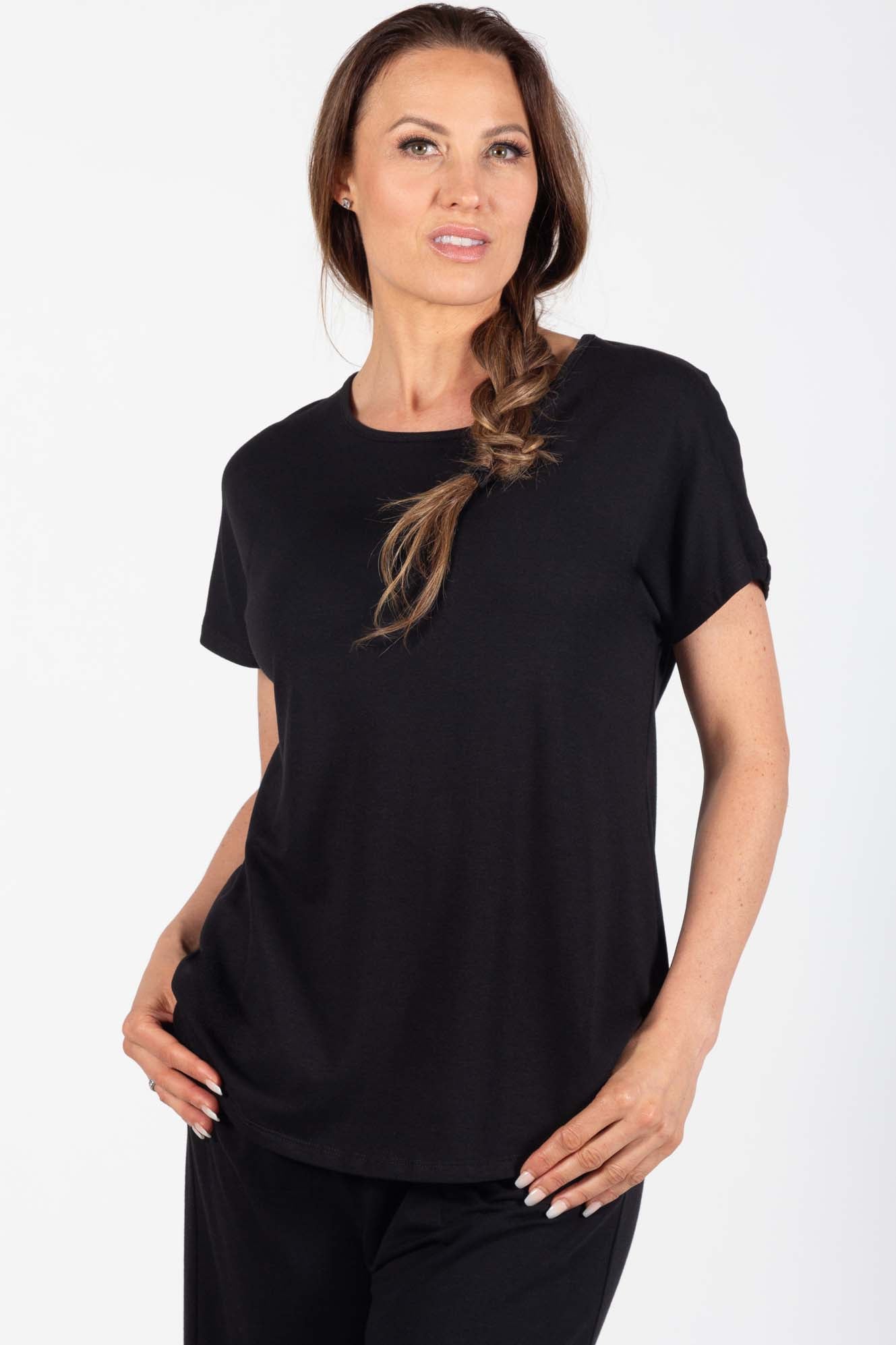 Woman wearing the Callie Top by Pure Essence in Black, a basic t-shirt, standing in front of a white background