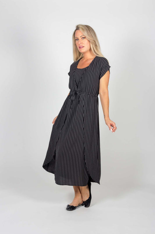 A woman wearing the Clementine Dress by Pure Essence in Black pinstripe stands in front of a white background