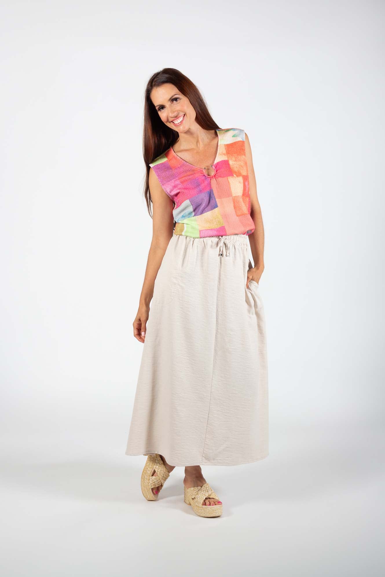 A woman wearing the Cole Skirt by Pure Essence in Sand with a pastel patchwork top, standing in front of a white background 