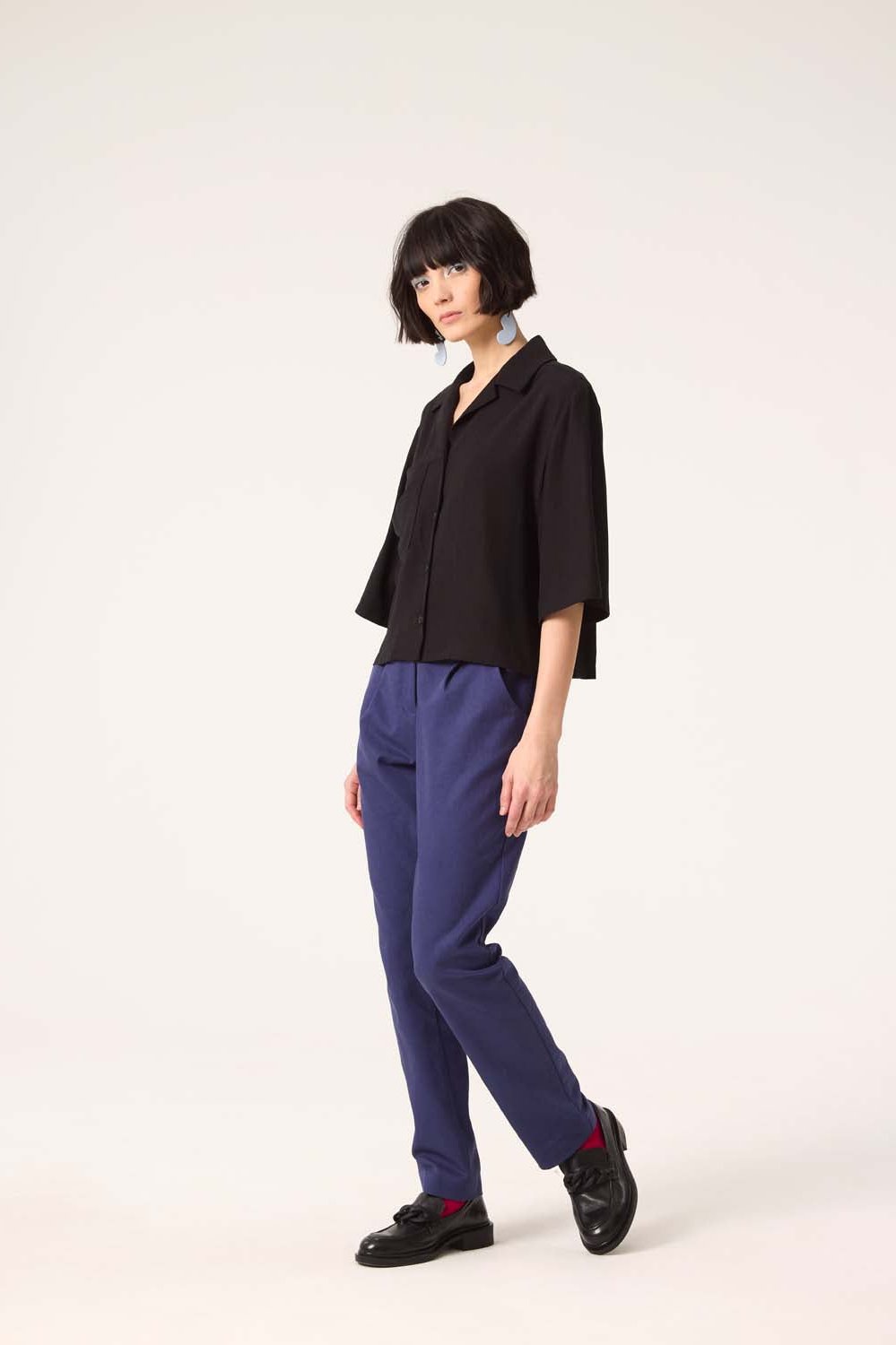 A woman wearing the Ritual Top by Cokluch in Black with blue pants, standing in front of a white background 