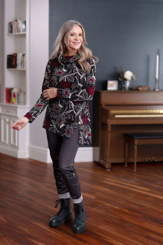 A woman wearing the Goya Pants by Rien ne se Perd in Grey, faux-denim leggings with an elastic waistband and decorative side pockets. She's wearing them with the Corno Tunic and standing in front of a piano. 