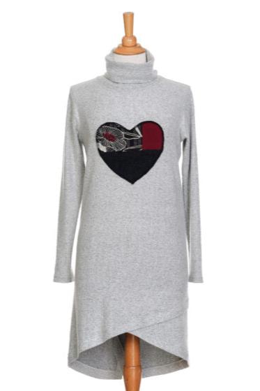 The Michelangelo Dress by Rien ne se Perd in Pale Grey, a long sleeved turtleneck dress with a heart applique on the front, is shown on a mannequin in front of a white background. 