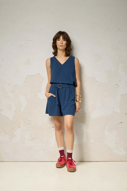 A woman wearing the Sita Top by Cokluch in Denim print, a sleeveless V-neck tank with a loose fit and wide straps. She is wearing it with matching shorts against a plain background