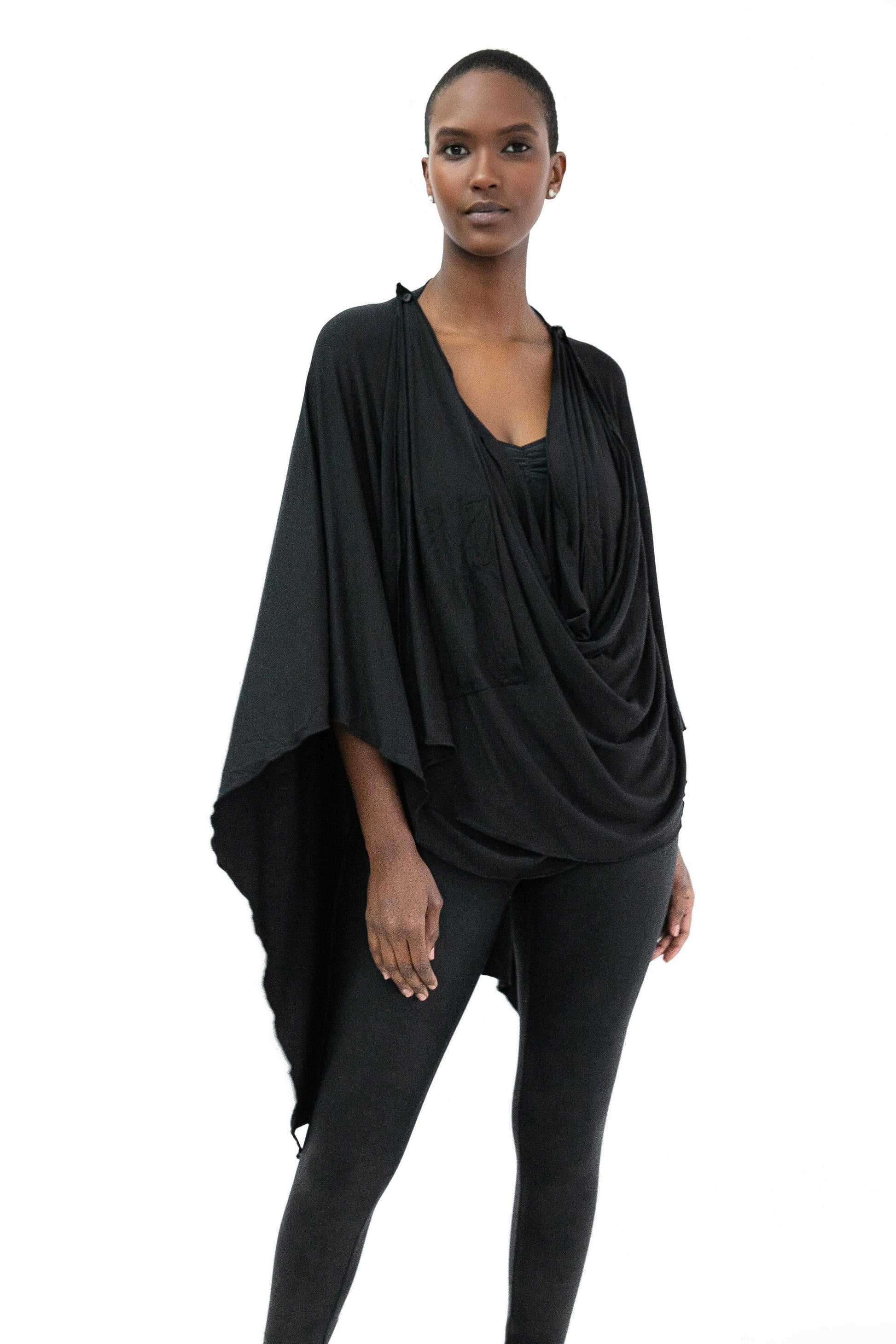 A woman wearing the Endless Bamboo Multi-wrap top by Stacey Martin Lifestyle in Black, a top that can be wrapped and fastened by the shoulder buttons in many different ways. She is wearing it with black leggings and standing against a white background. 
