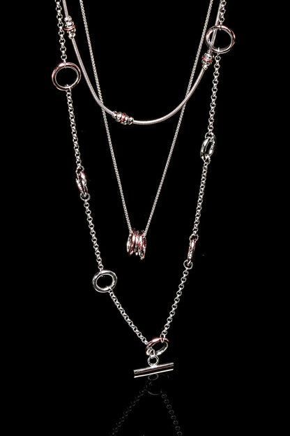 The Claudine Moncion Stack14 necklace is layered with other necklaces on a black background. 