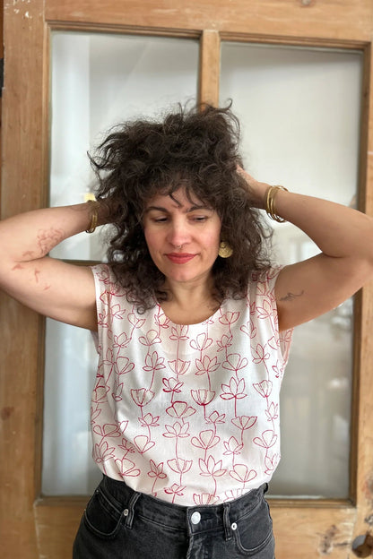 A woman wearing the wearing the Sandrigo Top from Kazak in Red Floral, a loose cotton top with short extended sleeves and a wide round neck. She is wearing it black jeans and standing in front of a wooden door. 