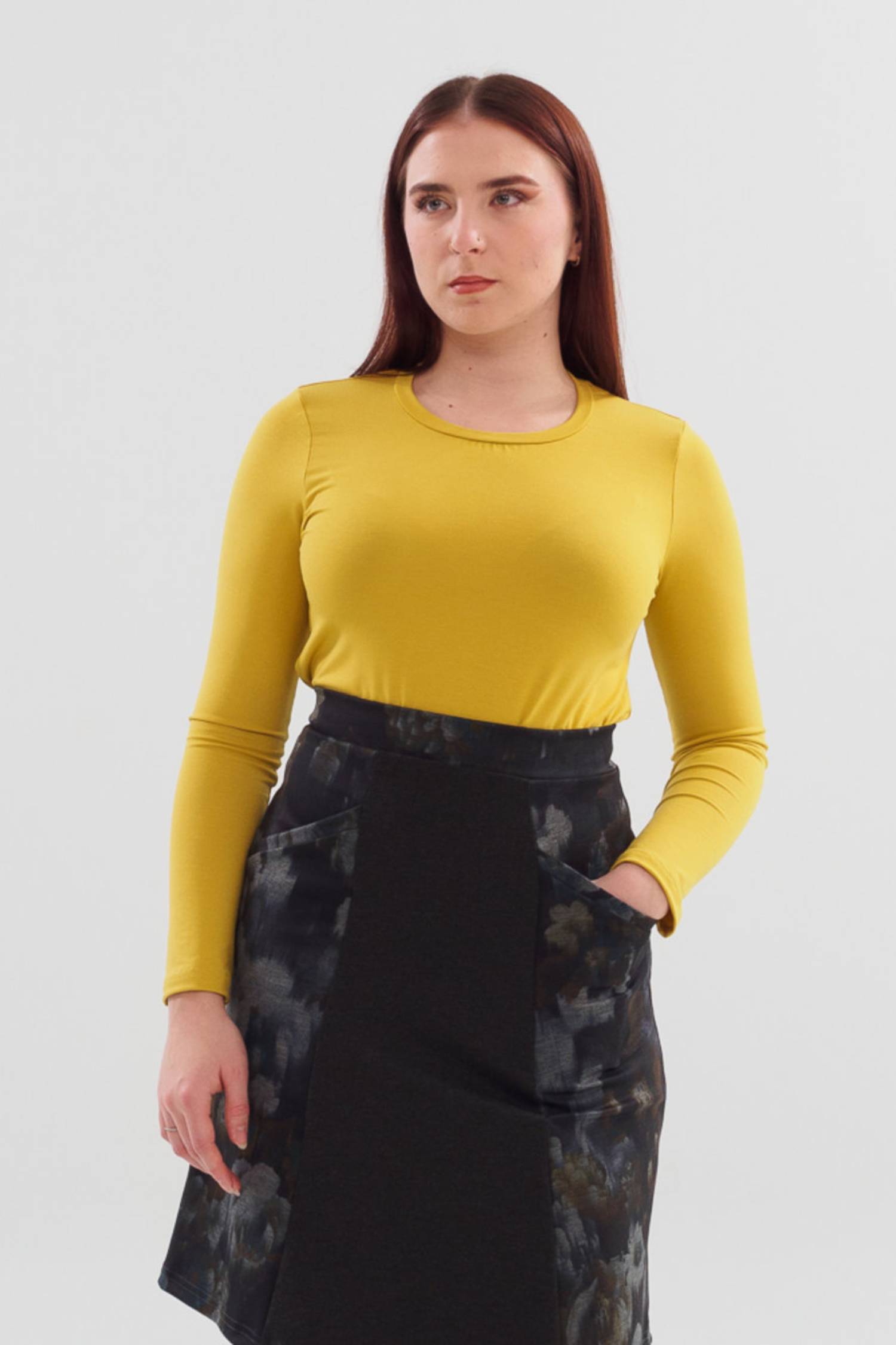 A woman wearing the A24 Top by Slak in Lemon, featuring long sleeves and a round neck,  standing in front of white background. 