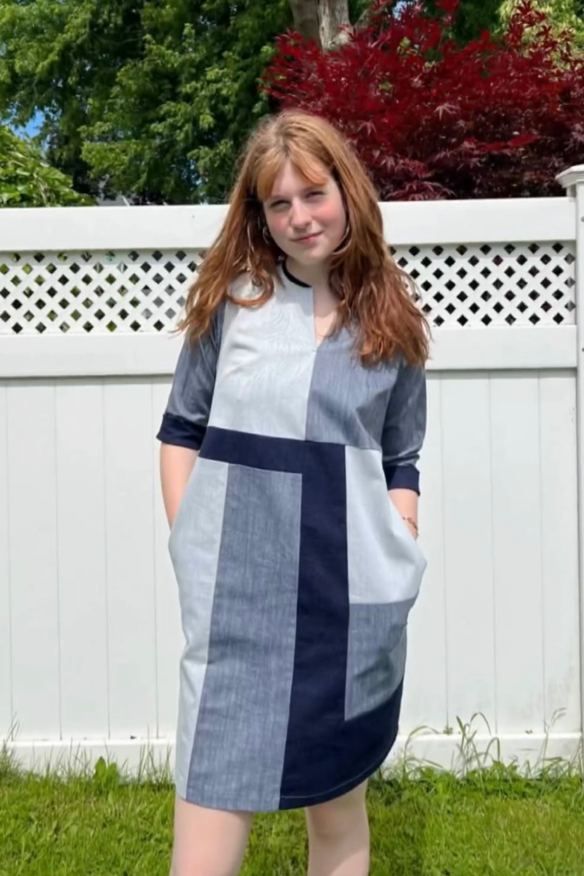 A woman wearing the Serena Dress by Solomia in Navy/Grey/White colourblocking, standing in front of a white fence