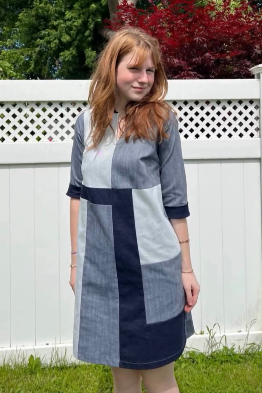 A woman wearing the Serena Dress by Solomia in Navy/Grey/White colourblocking, standing in front of a white fence