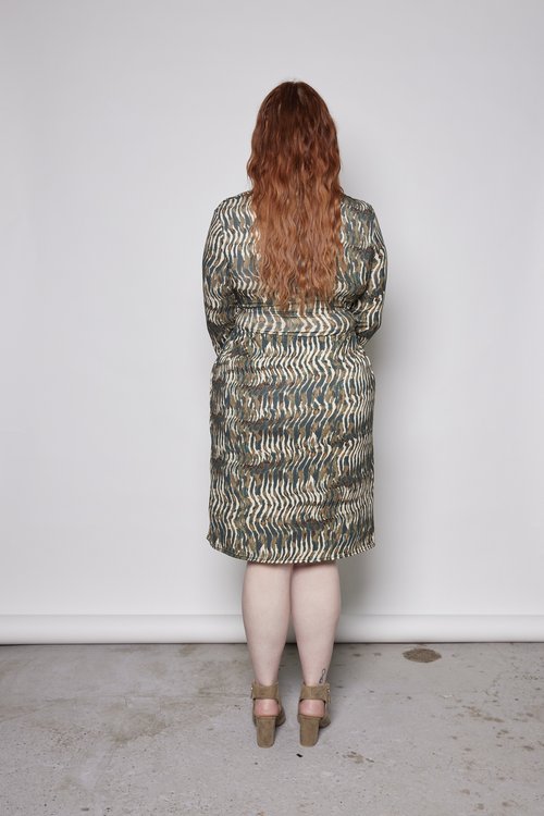 Back view of a woman wearing the Gwen Dress by Tangente in Green print, standing in front of a white background 