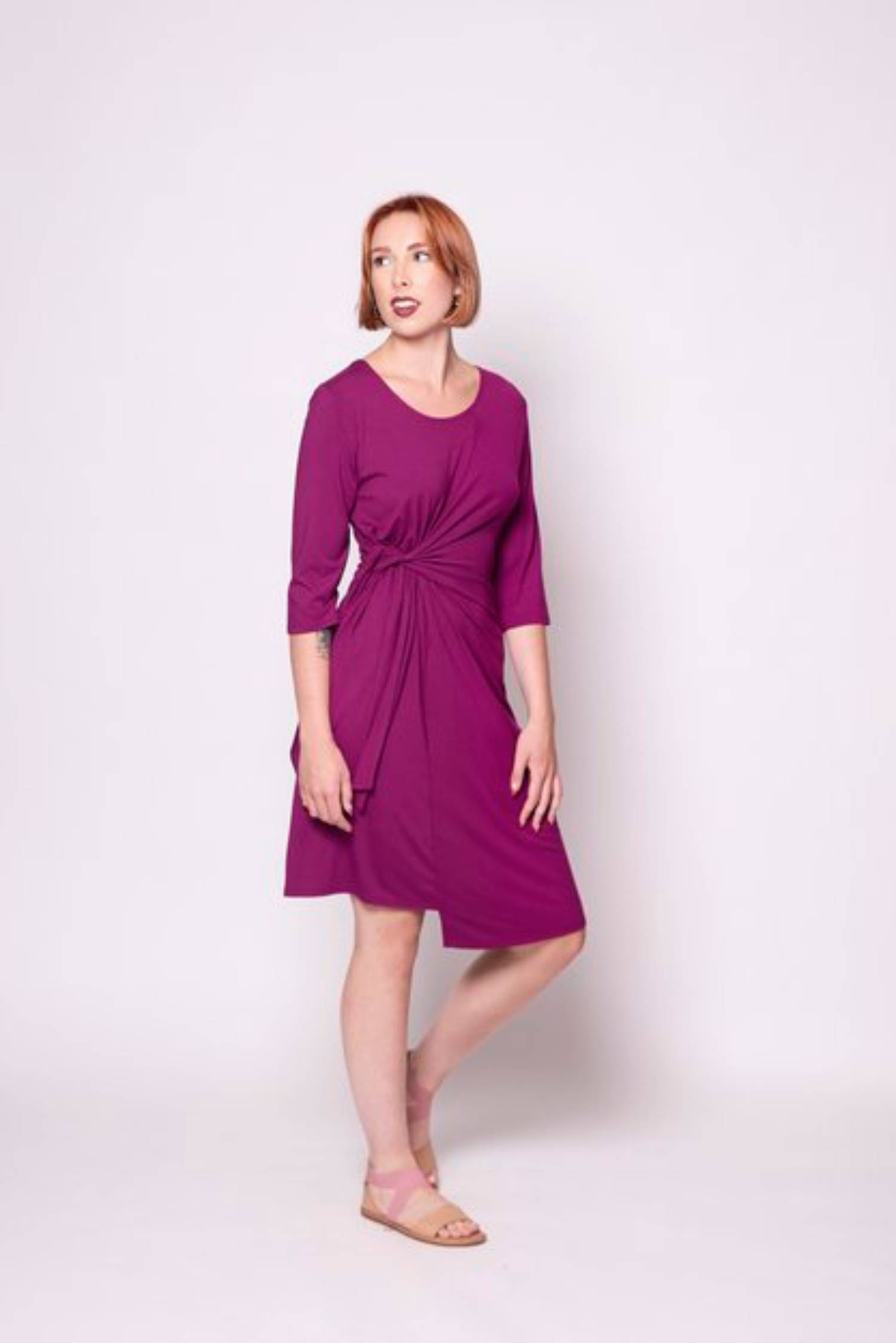 Side view of a woman wearing the Mariela Dress by Tangente in Fuschia, standing in front of a white background 