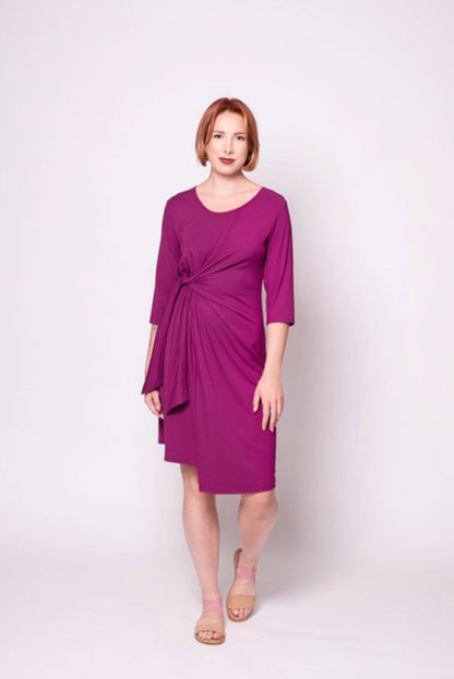 A woman wearing the Mariela Dress by Tangente in Fuschia, standing in front of a white background 