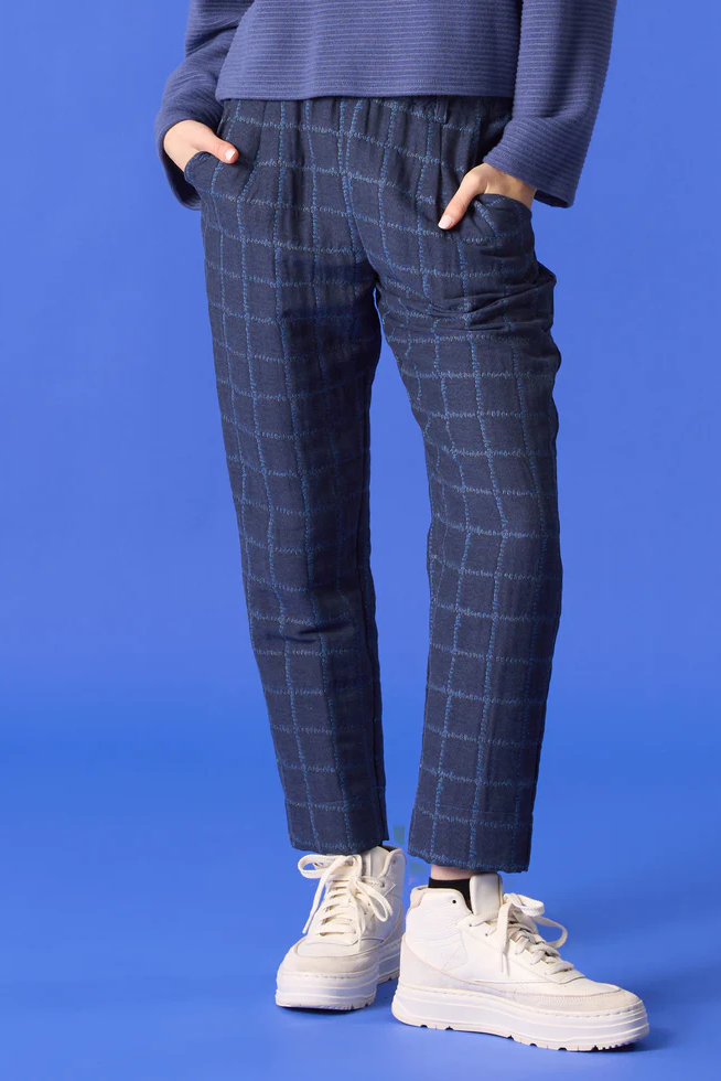 Waist-down view of a woman wearing the Vega Pants by Cokluch in Denim, featuring an exclusive checked jacquard fabric and slim ankle-length legs and a pull on waist. 