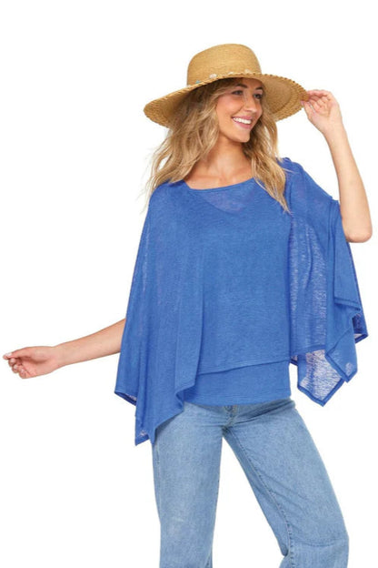 3/4 shot of a woman wearing the Centos Cami and Cathiana Poncho by Yul Voy in Blue, a lightweight knit tank with a v-neck and wide straps and a light poncho with a wide neck and asymmetrical hem. 