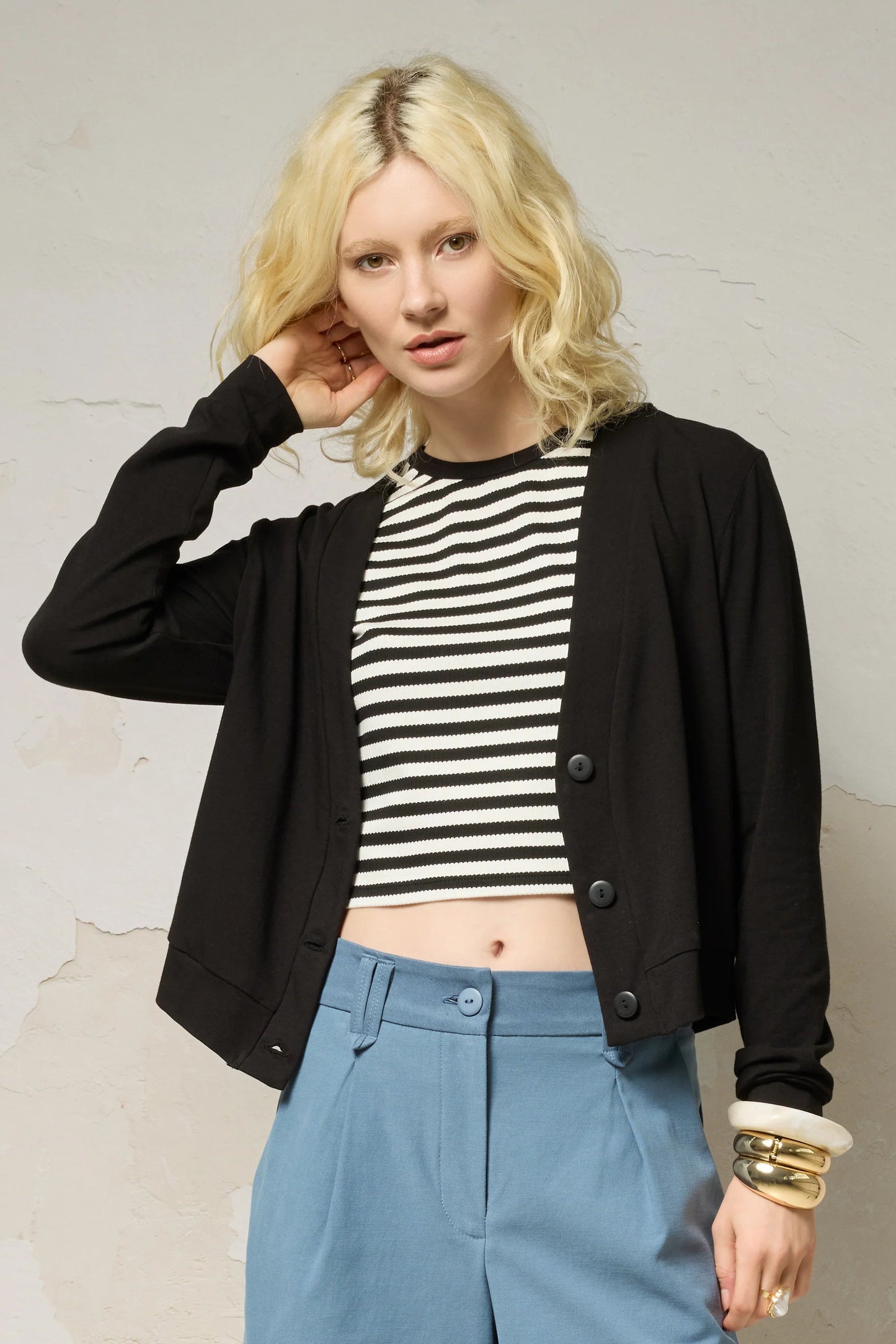 Waist up view of a woman wearing the Zephyr Cardigan by Cokluch in Black, a long sleeved waist length cardigan with a v-neck and four buttons. She is wearing it with the Hebe striped tank and blue shorts against a plain background. 