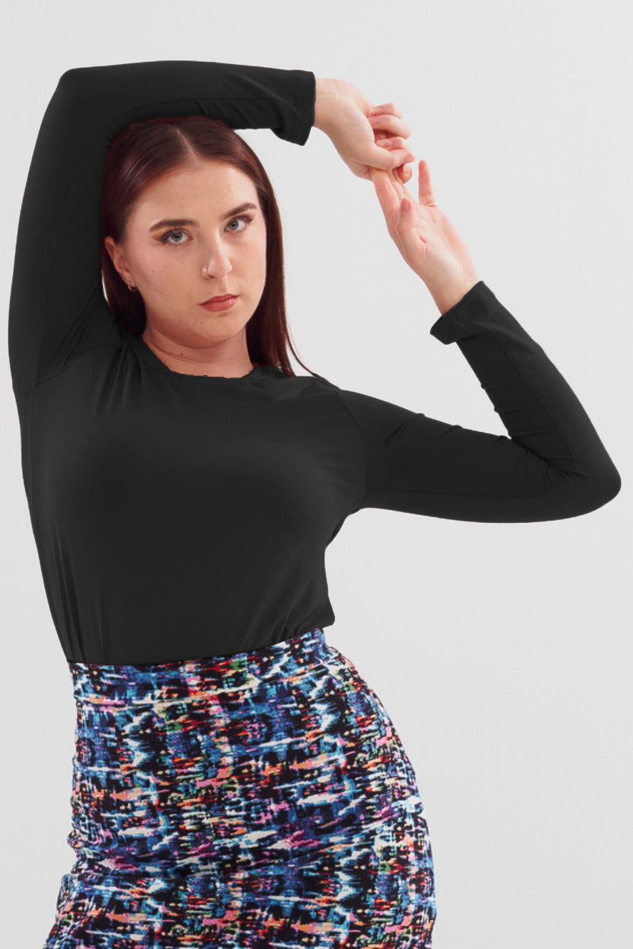 A semi close-up of a woman wearing the A24 Sweater by Slak in Black with the Eve Skirt, standing in front of a white background 