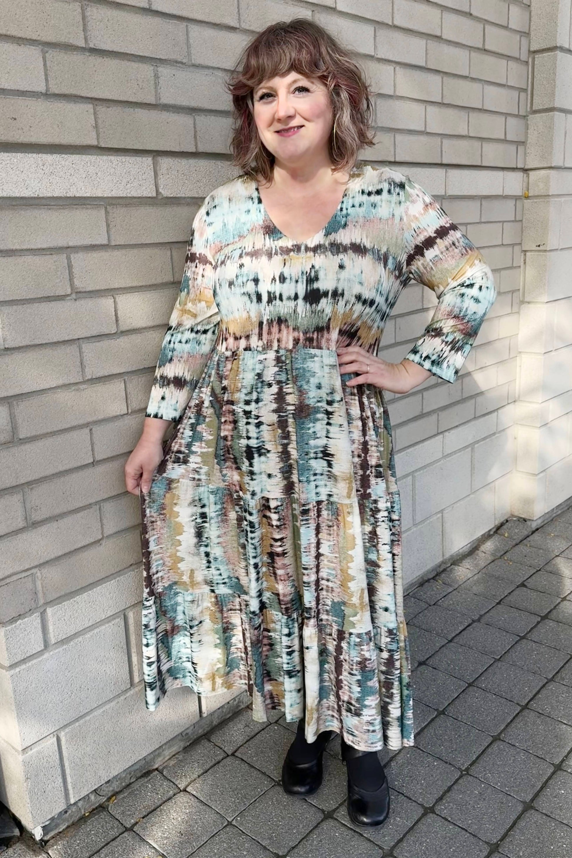 A 3/4 shot of a woman wearing the Denver Dress by Pure Essence in Multicolour Print, with a V-neck, long sleeves, gathered waist, and long tiered skirt 