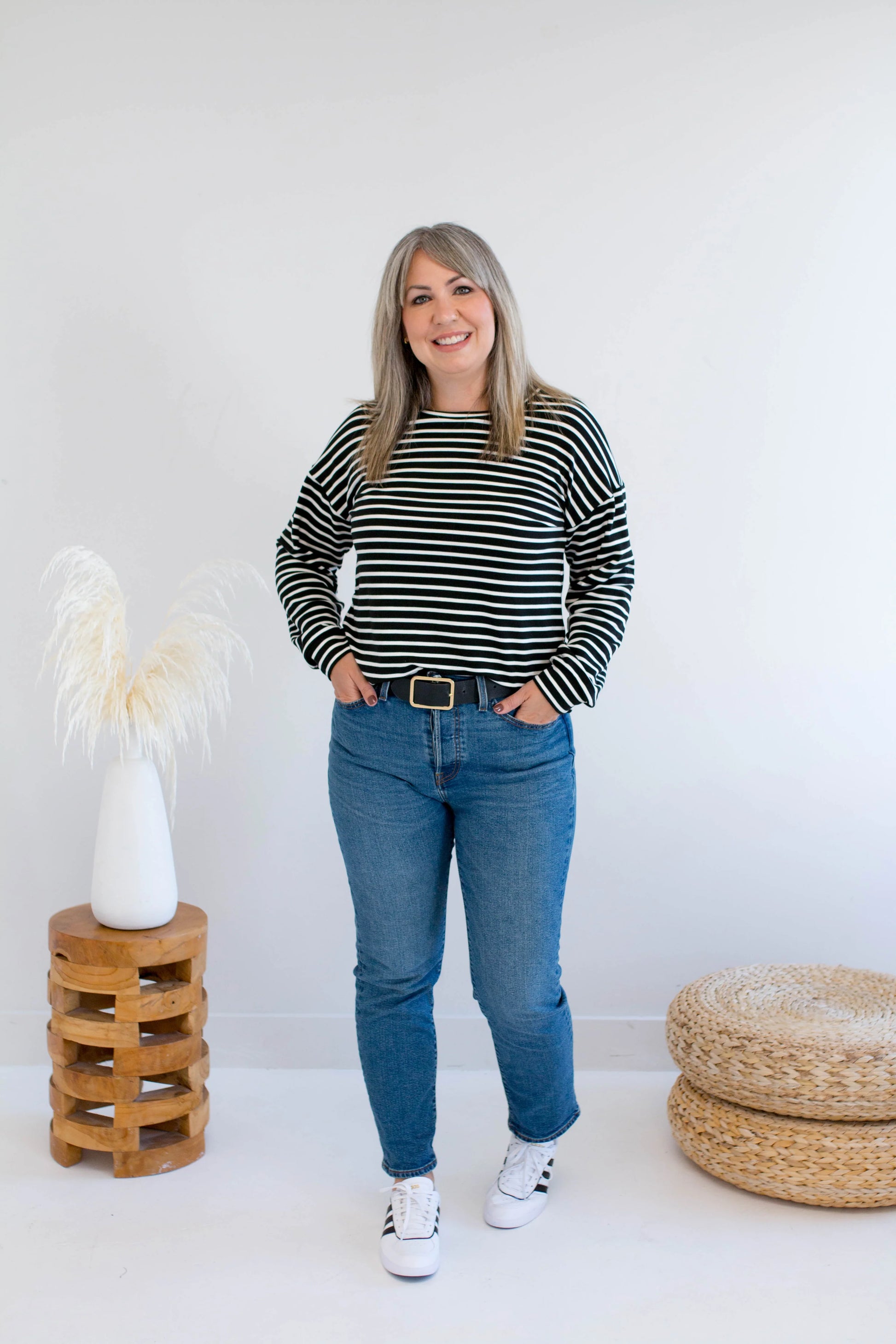 A woman wearing the Munro Bamboo Crewneck sweater by Ang Hill in black and white stripes. She is wearing it with jeans against a white background.