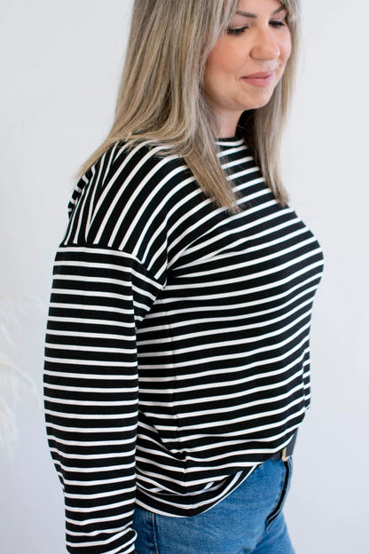 Side view of a woman wearing the Munro Bamboo Crewneck sweater by Ang Hill in black and white stripes. She is wearing it with light blue jeans against a white background.