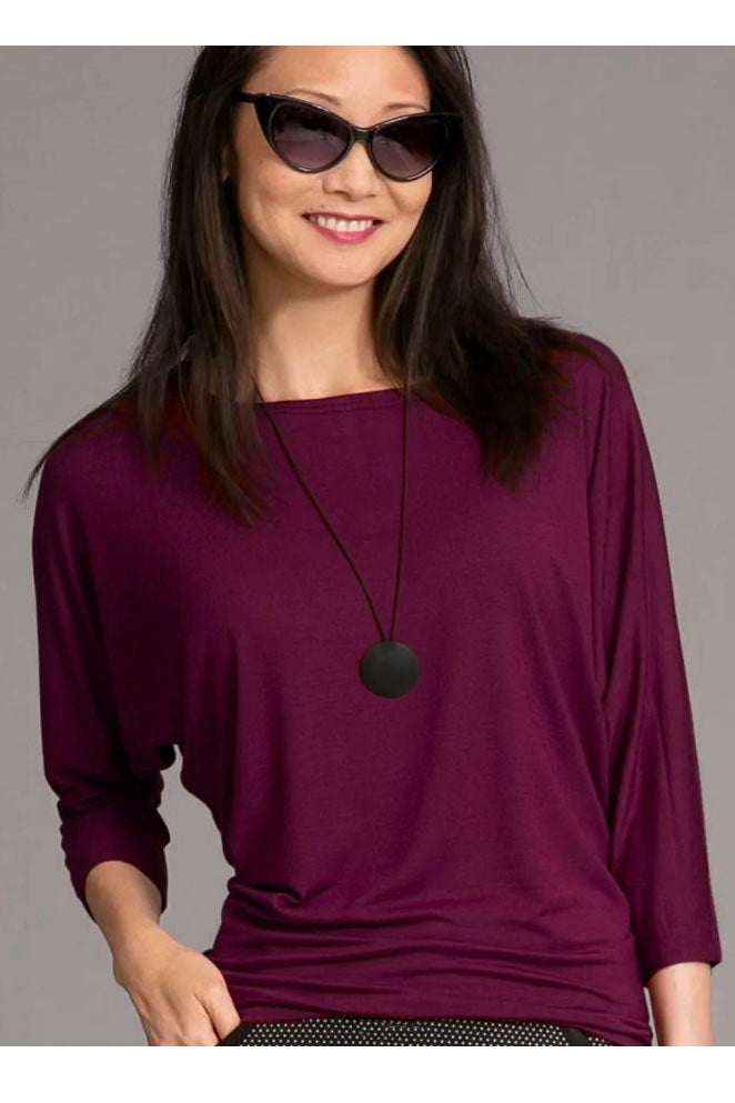 A woman wearing the Jo Slouch Tee by Mandala in Mulberry, standing in front of a grey background 
