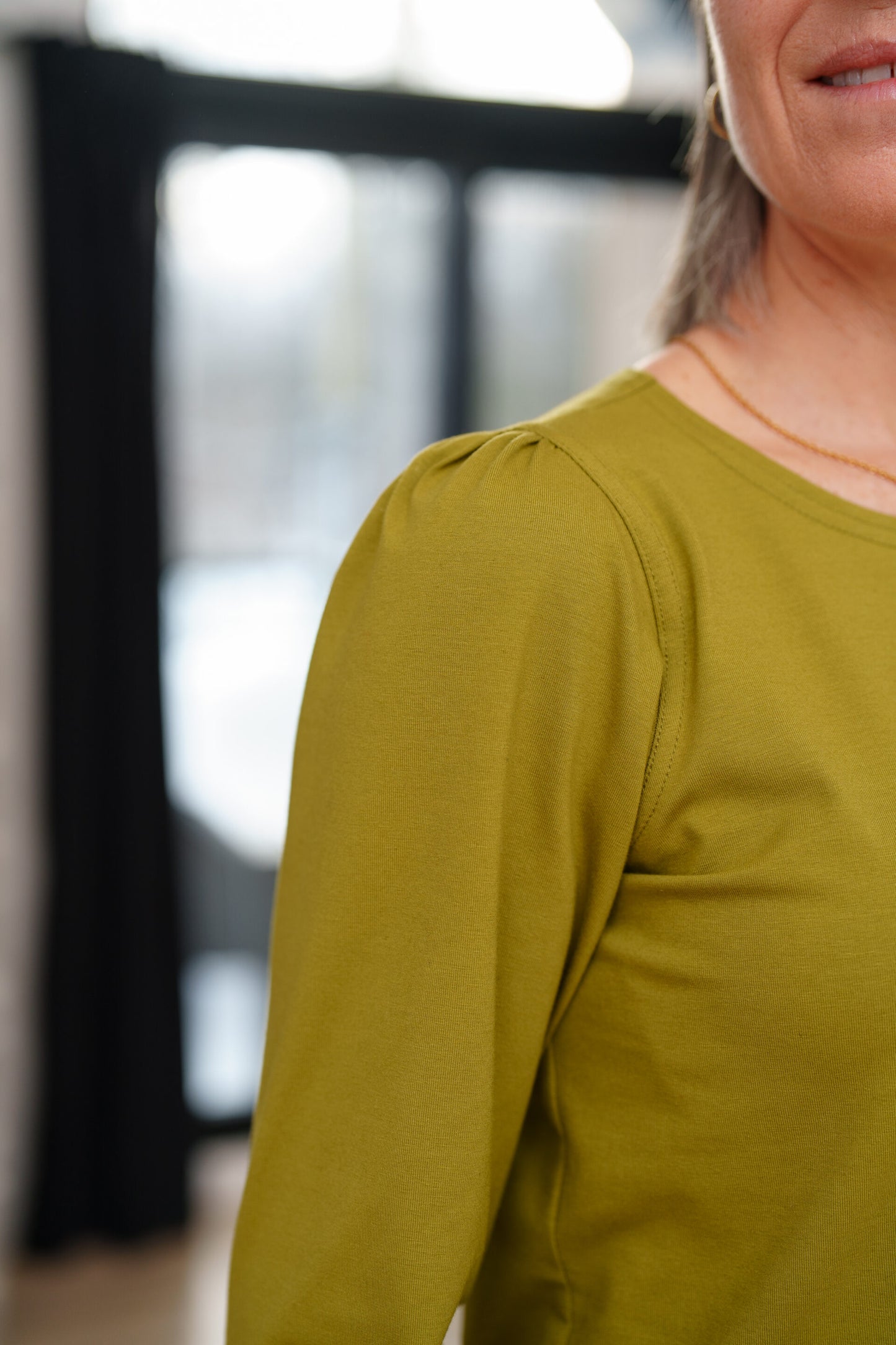 Close up of a woamn  wearing the Becancour Top by Rien ne se Perd in Pistachio, with a round neck and long slightly puffed sleeves with gathered cuffs.