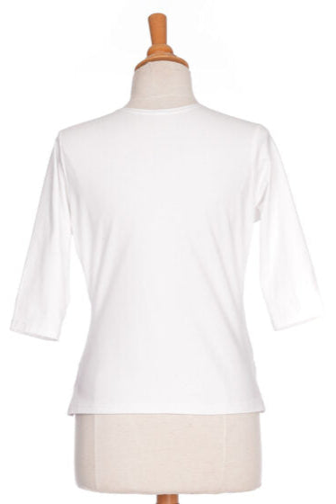 A back view of the Cotillon Top by Rien ne se Perd in White, a v-neck top with a wrap-over front, coconut shell buckle at the waist, and 3/4 sleeves, made from stretch cotton, is show on a mannequin in front of a white background. 