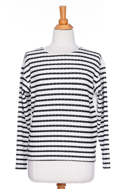 The Collins Reversible Sweater by Rien ne se Perd in Black/White is shown on a mannequin agains ta white background. t's reversible back to front with stripes on side and solid fabric on the other. It has long striped sleeves and a round neck. 