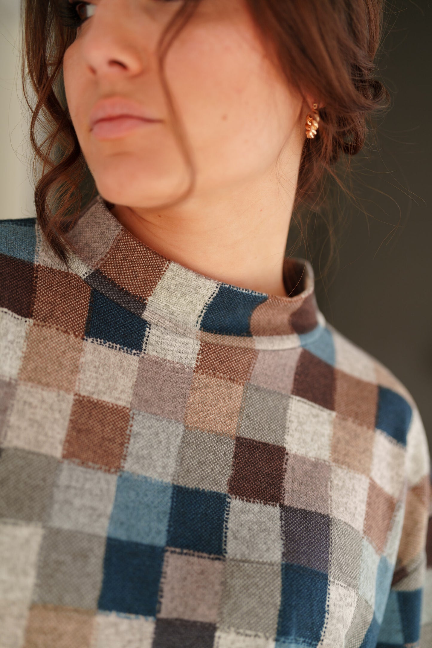 Close up detail of a woman wearing the Leran Sweater by Rien ne se Perd in Checkered print, a mock-neck knit sweater with a blue, brown, and beige pattern.