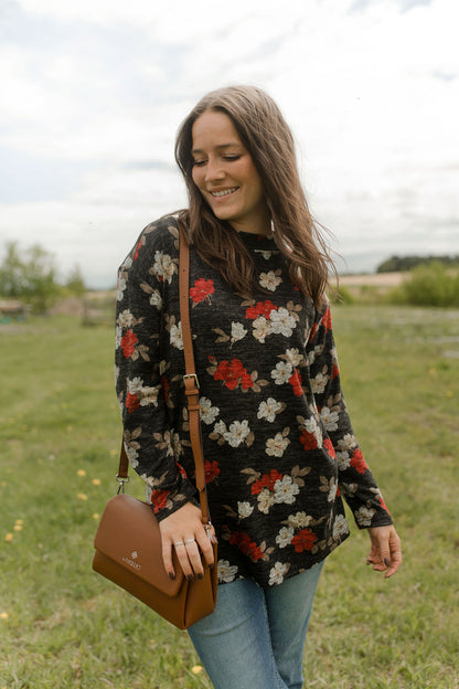 A woman wearing the Leran Sweater by Rien ne se Perd in Floral print, a mock-neck knit sweater with a black, white and red pattern. She is wearing it with jeans and standing outside in a field. 