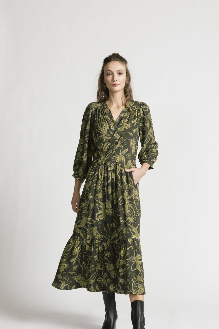 A woman wearing the Chatterley Dress by Allison Wonderland in Green Floral, standing in front of a white background 