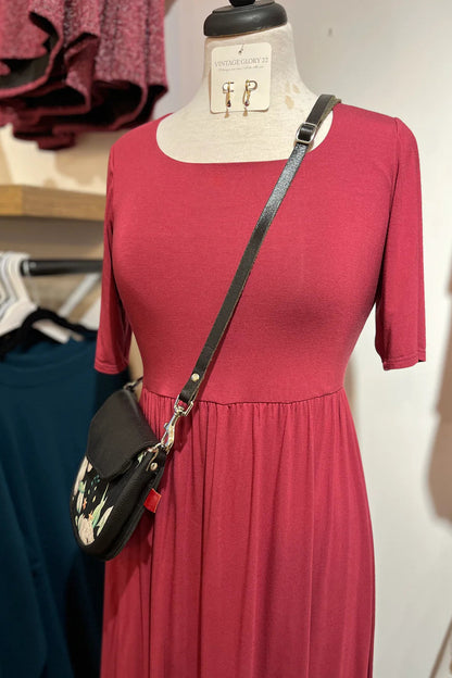 The Doppio Dress by Cherry Bobin in Red with slight scooped neck, half sleeves, a fit and flare shape, and full skirt that falls below the knee, is showon a mannequin in a clothing store.