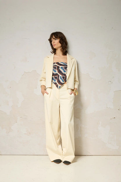A woman wearing the Vesta Jacket by Cokluch in Vanilla over a patterned top and matching pants against a plain background