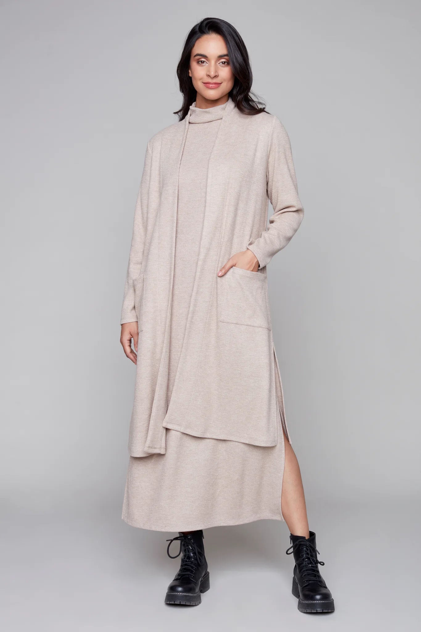 A woman wearing the Naomi Knit Top in by Compli K in Beige, a long open cardigan with patch pockets and side slits, over a matching dress