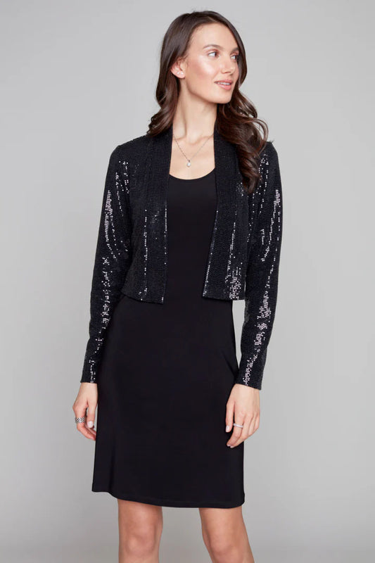 A woman wearing the Nova Bolero by Compli K in black, a sequined waist-length bolero with long sleeves, over a black dress