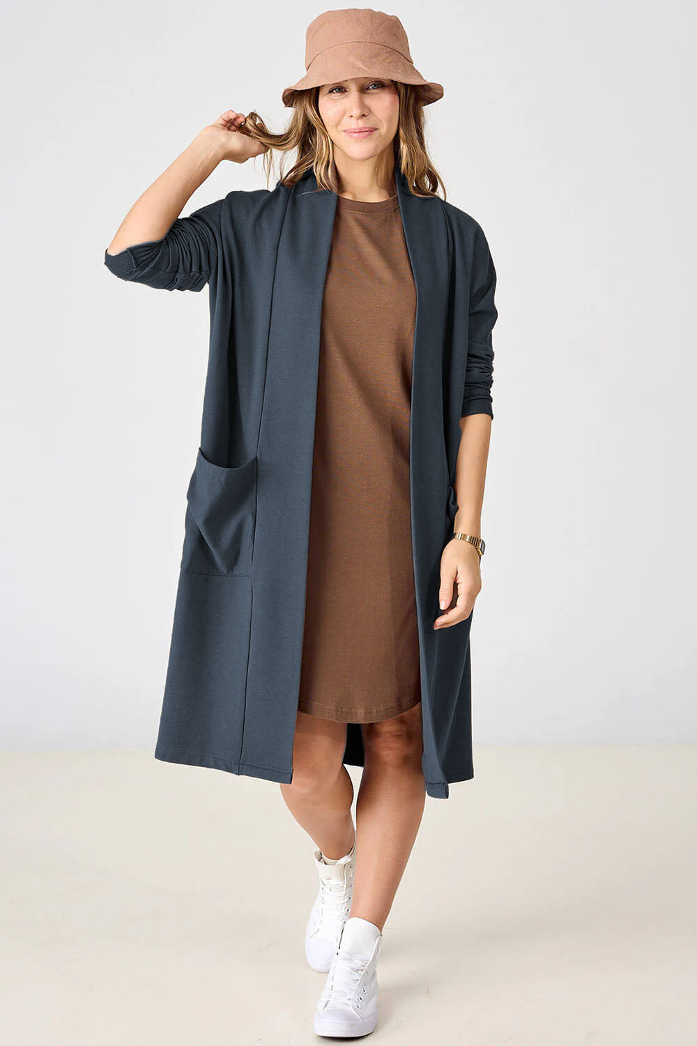 A woman wearing the Courtney Cardigan by Advika in Blue Steel, a long open cardigan with  patch pockets made from tencel/organic cotton eco-fabric, over a tan dress