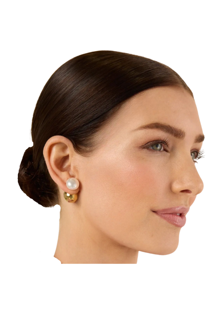 A close-up side profile of a woman with dark hair in a low bun, wearing 
the HoopLa Pearl and Gold Ball earring s