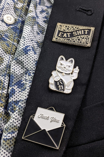 The Fuck You Pin by Badaboöm Studio is shown along with other sassy pins on a black suit lapel.