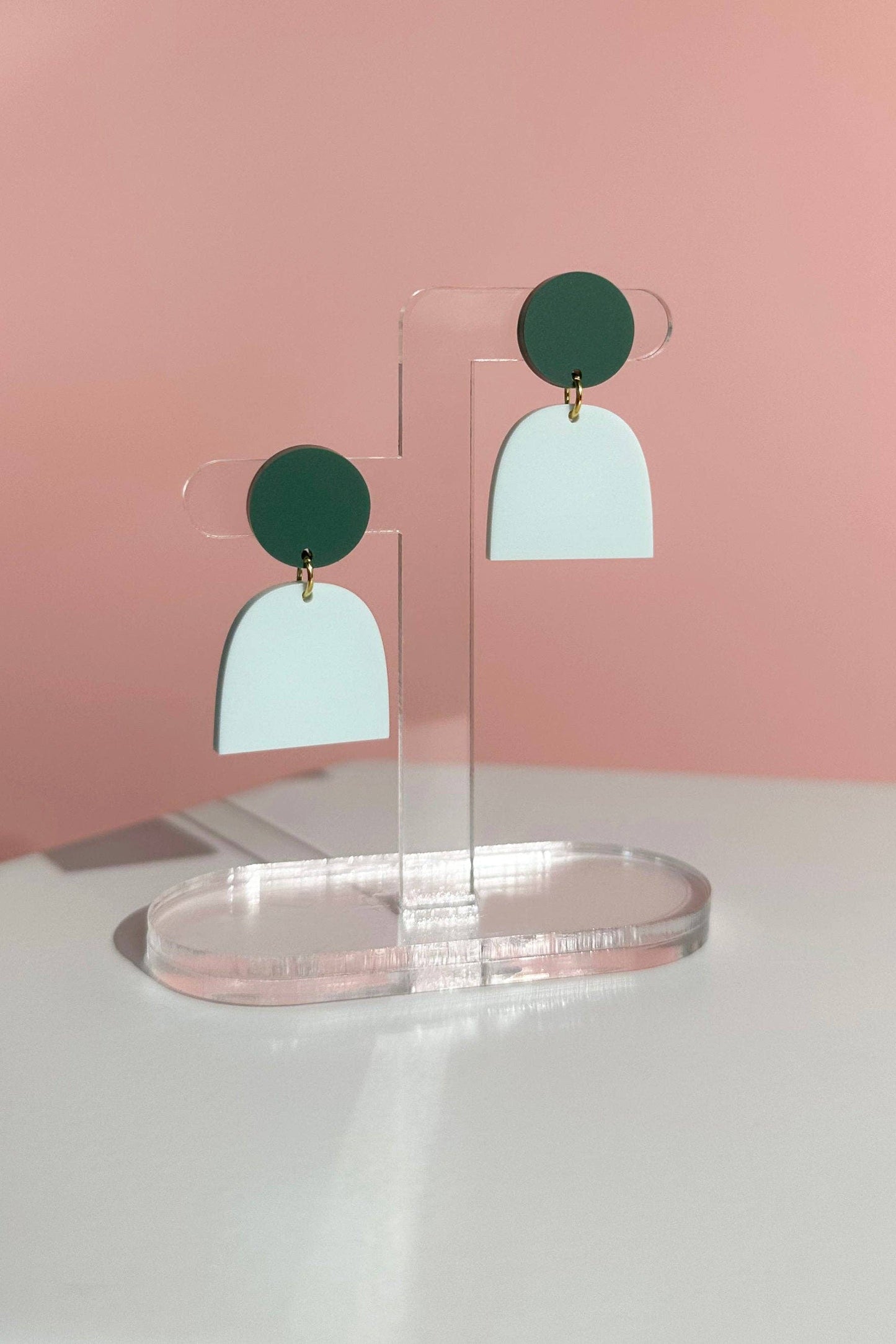 Pair of earrings on a clear stand against a pink background