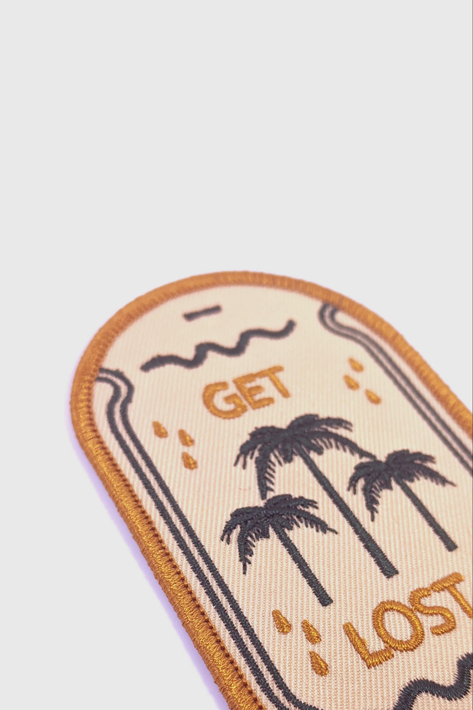 Embroidered Badaboöm studio patch with palm trees and 'Get Lost' text on a beige background