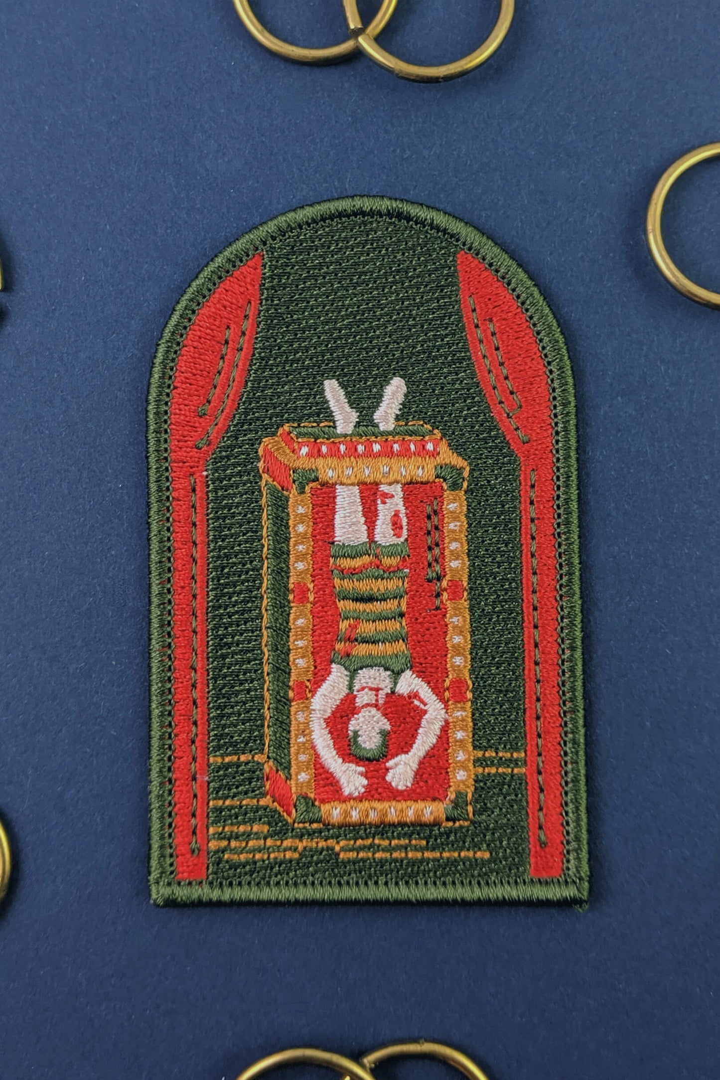 An embroidered arched patch from Badaboöm Studio showing Houdini upside down in a water tank, show against a navy background. 