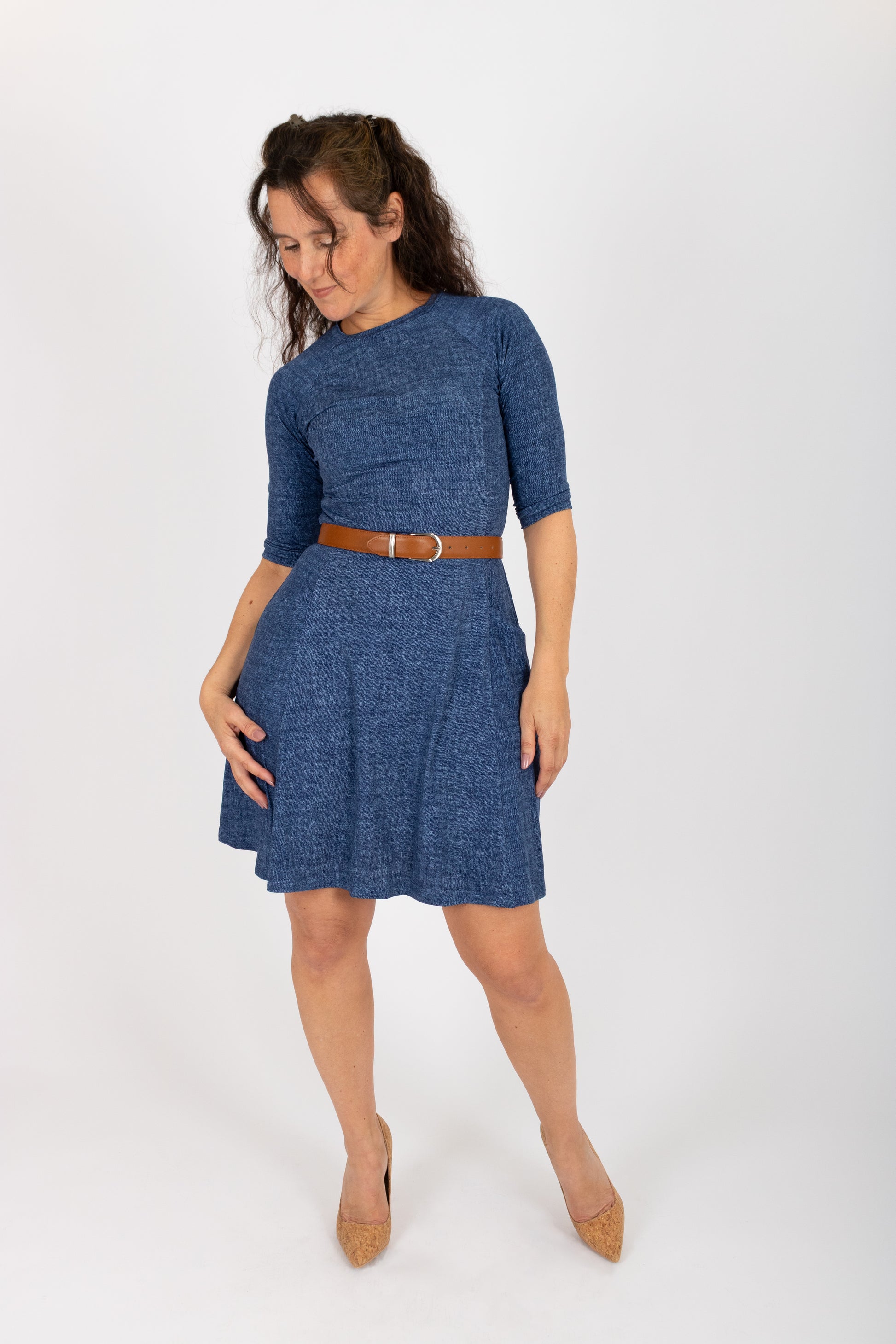 A woman wearing the Raphaelle Dress from Infime in Blue, an A-line knee-length dress with 3/4 raglan sleeves and pockets. She is standing in front of a white background.