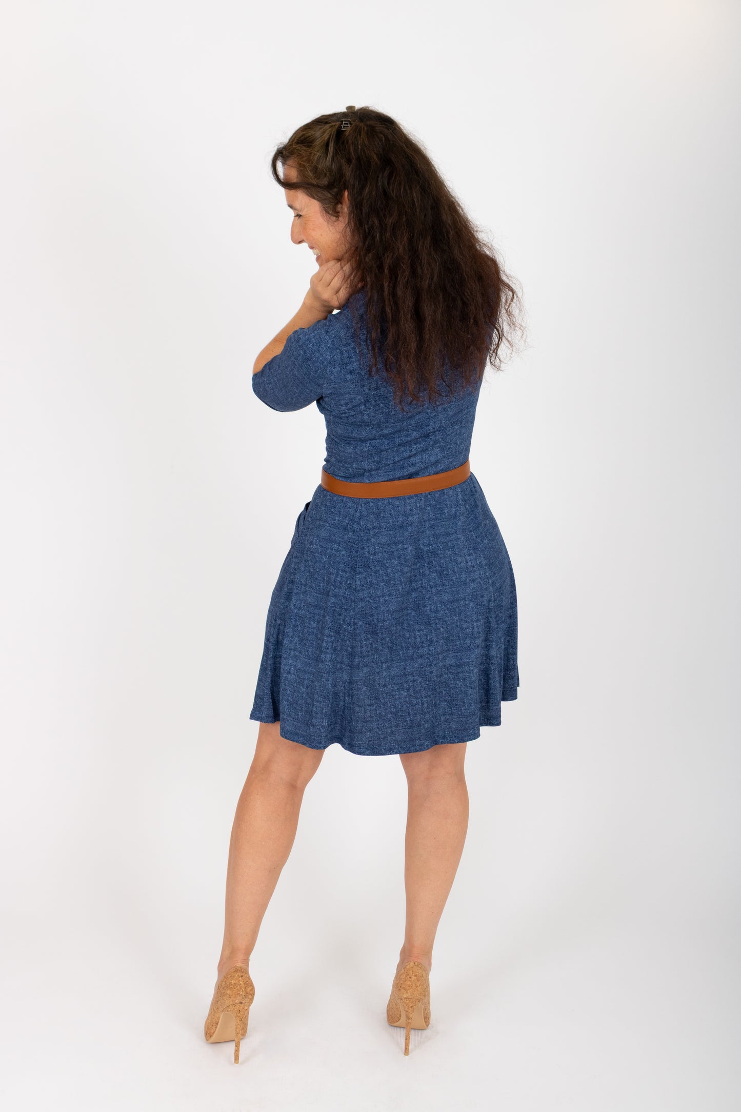 Back woman wearing the Raphaelle Dress from Infime in Blue, an A-line knee-length dress with 3/4 raglan sleeves and pockets. She is standing in front of a white background.