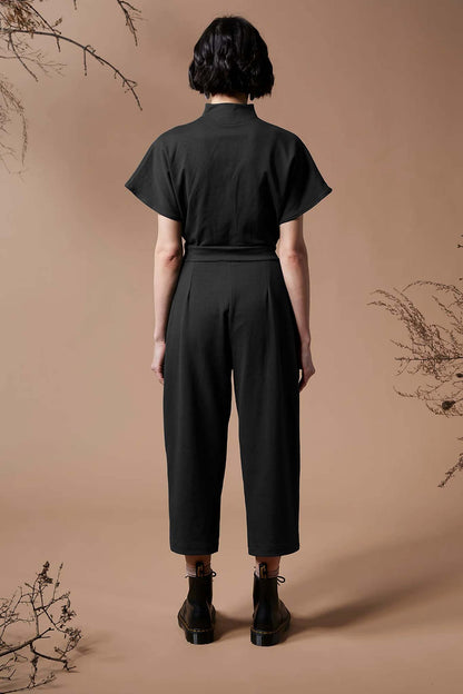 Back view of a woman wearing the Jayden Jumpsuit by Melow in Black, standing in front of a beige background